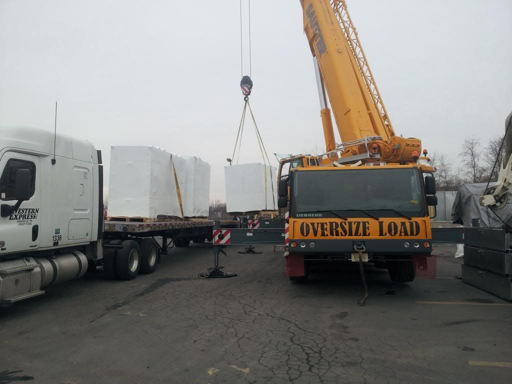Huge crane loading pallets onto a flatbed truck in a parking lot
